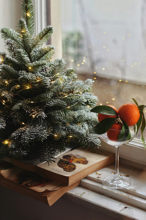 Un árbol de Navidad junto a un libro y un cuenco con naranjas