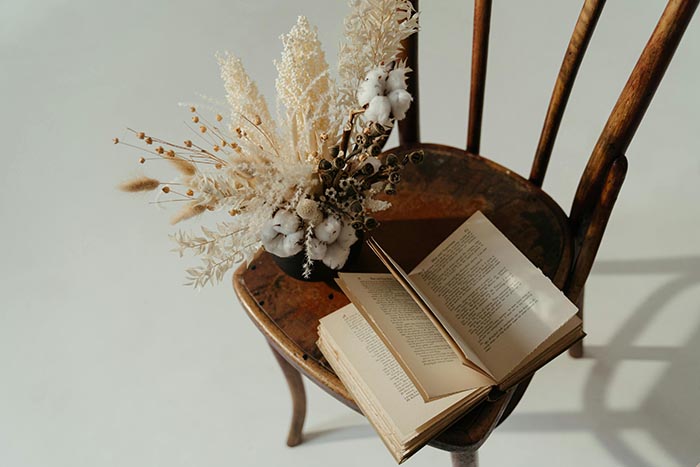 Un libro reposando en una silla de madera junto a un ramo de flores secas